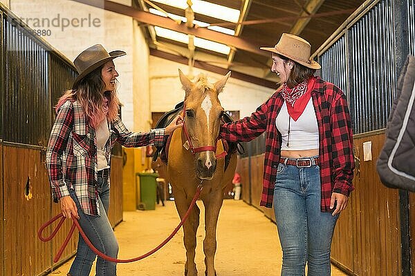 Zwei Cowgirl Frauen haben Spaß und lachen mit einem Pferd  mit südamerikanischen Outfits  Lebensstil von zwei Frauen arbeiten in einem Stall