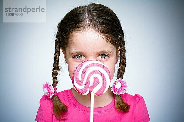 Ein junges Mädchen hält einen großen spiralförmigen Lollypop  während es rosa gekleidet ist