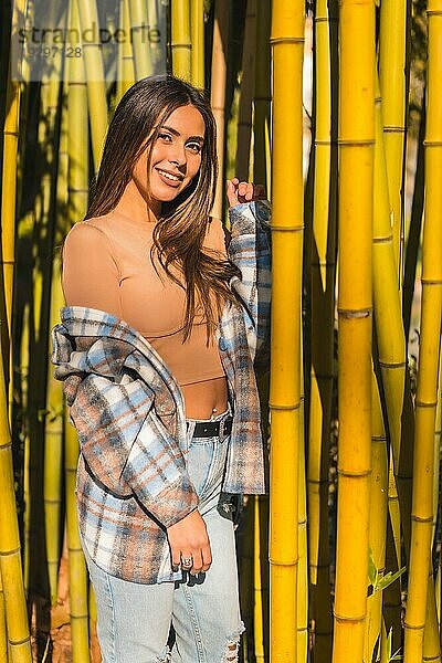 Herbstlicher Lebensstil  junges kaukasisches brünettes Mädchen in einem karierten Wollpullover  lächelnd in einigen Bambusbäumen