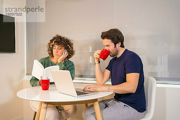 Lifestyle  ein junges kaukasisches Paar im Schlafanzug beim Frühstück in der Küche  ein Mädchen  das ein Buch liest  und ein Junge  der E Mails am Computer liest