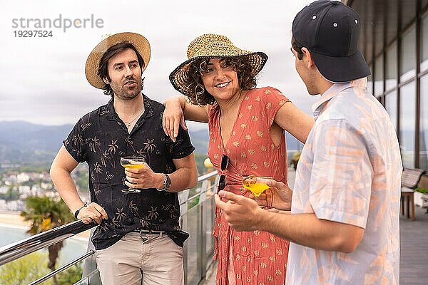 Horizontales Foto von drei Freunden  die auf einer Terrasse im Sommer Cocktails trinken