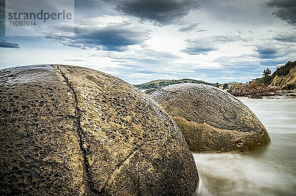 Nahaufnahme der runden Felsformationen der Moeraki Boulders in Moeraki  Neuseeland. Die Langzeitbelichtung fängt die Bewegung der Wolken und Wellen um die Felsen ein