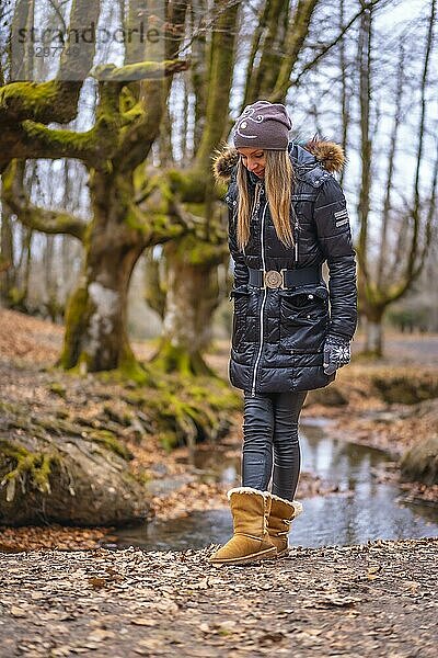 Blondes Mädchen lächelnd in einem Wald mit Wintermütze im Herbst
