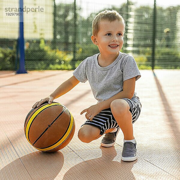Fröhlicher Junge spielt Basketball im Freien