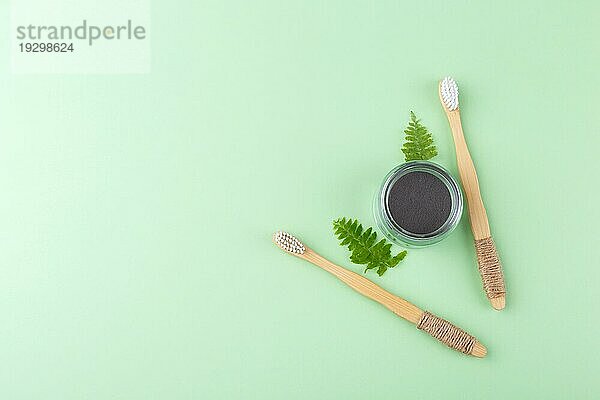 Natürliche Bambuszahnbürsten und schwarzes Zahnpulver auf grünem Hintergrund  Null Abfall Produkte  natürliche Mundhygiene