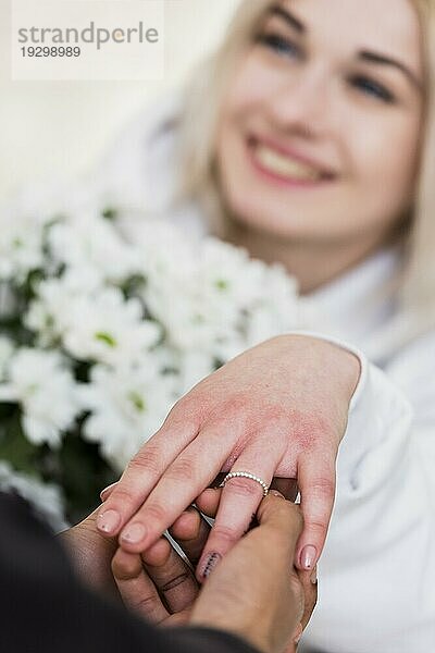 Mann legt diamantenen Verlobungsring an den Finger seiner Verlobten