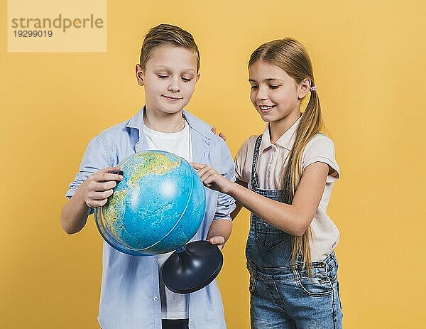 Close up lächelnde Mädchen berühren Globus halten von ihrem Freund stehen gegen gelben Hintergrund