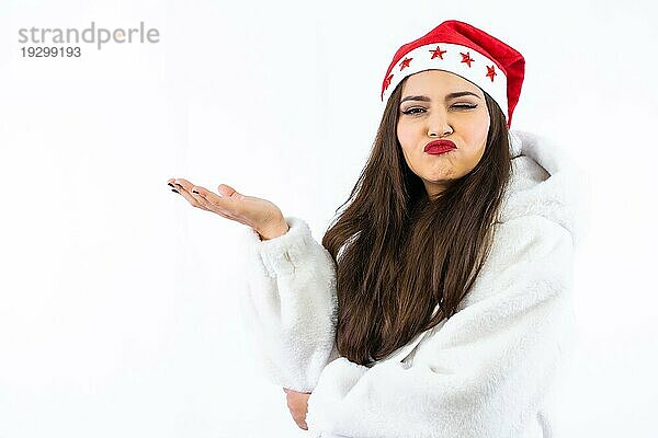 Lateinisches brünettes Mädchen an Weihnachten mit weißem Hintergrund  mit einer Weihnachtsmütze mit Sternen  Porträt mit Blick in die Kamera und Zwinkern  Kopierraum