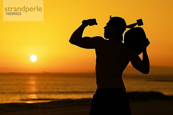 Silhouette eines fitten Mannes mit Bizeps vor dem Hintergrund eines hellen Sonnenuntergangs. Mittlere Aufnahme