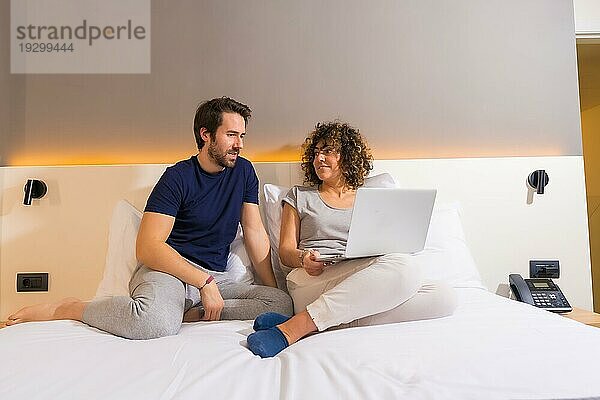 Lifestyle  ein heterosexuelles kaukasisches Paar im Schlafanzug auf dem Bett  das eine Online Reservierung auf dem Computer betrachtet