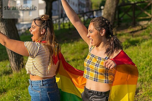 Eine Nahaufnahme von zwei jungen kaukasischen umarmen Frauen mit LGBT Stolz Flagge im Freien