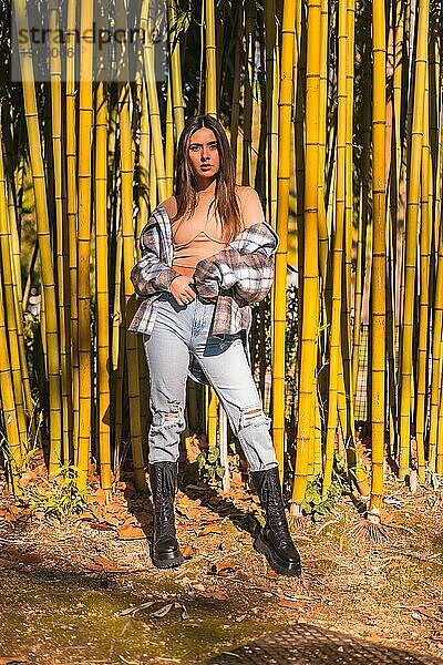 Herbstlicher Lebensstil  junges kaukasisches brünettes Mädchen in einem karierten Wollpullover und zerrissenen Jeans in einem Bambushain