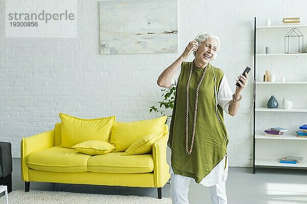 Lächelnde ältere Frau hört Musik über Kopfhörer mit ihrem Mobiltelefon