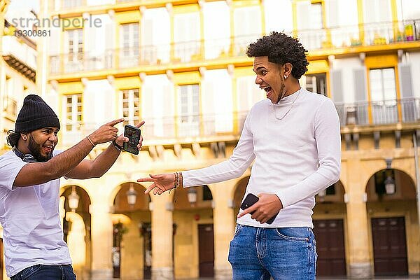 Lifestyle  zwei schwarze Latino Freunde  die sehr glücklich sind  sich lange Zeit später auf der Straße zu treffen. Junge mit Afrohaar und Junge mit Hut und Kopfhörer