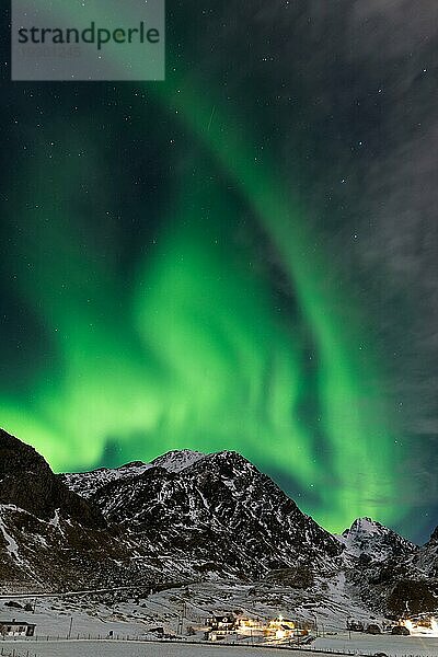 Spektakuläres tanzendes grünes starkes Nordlicht über dem berühmten runden Sandstrand bei Haukland auf den Lofoten in Norwegen in einer klaren Winternacht mit schneebedeckten Bergen