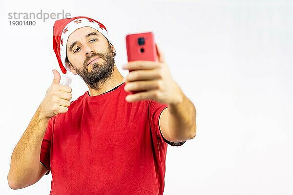 Sehr glücklicher junger kaukasischer Mann mit roter Weihnachtsmütze  der ein Selfie auf weißem Hintergrund macht  bekleidet mit einem roten TShirt Copy Paste