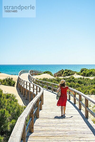 Mädchen mit rotem Kleid auf dem Holzweg zum Playa Moncayo in Guardamar del Segura bei Torrevieja  Alicante. Gemeinschaft von Valencia. Spanien  Urlaub am Mittelmeer
