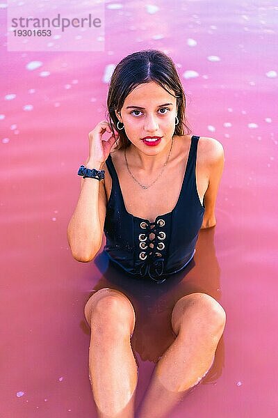 Posing einer jungen brünetten Kaukasierin im Sommerurlaub in der rosa Lagune von Torrevieja  die mit verführerischem Blick im Wasser sitzt  Alicante. Spanien