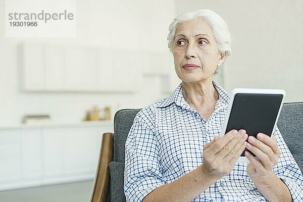 Ältere Frau hält digitales Tablet und schaut weg
