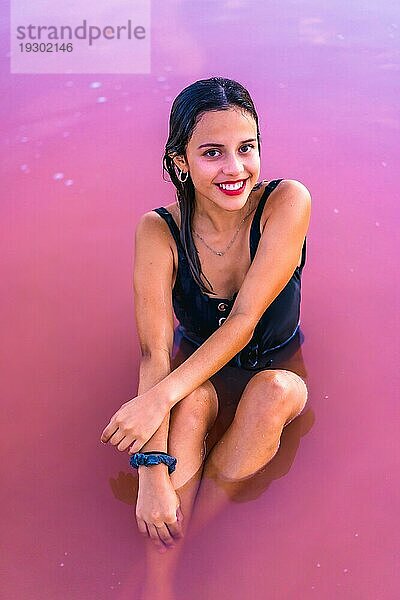 Posing einer jungen brünetten Kaukasierin im Sommerurlaub in der rosa Lagune von Torrevieja  die lächelnd im Wasser sitzt  Alicante. Spanien
