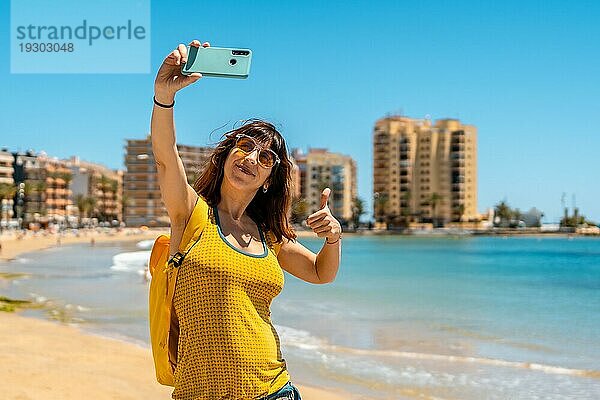 Eine sehr glückliche junge Frau macht ein Selfie mit dem Handy in Playa del Cura in der Küstenstadt Torrevieja  Alicante  Valencianische Gemeinschaft. Spanien  Mittelmeer
