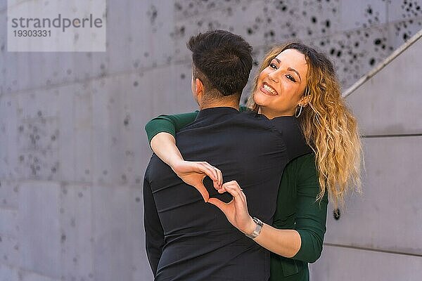 Modische Pose eines kaukasischen Liebespaares in einem blauen Anzug und einem grünen Kleid  das sich umarmt und mit den Händen ein Herz bildet