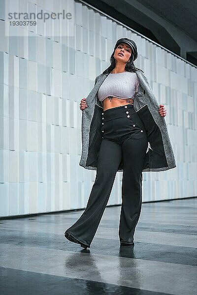 Modisches Posieren in der Stadt eines wunderschönen Latino Mädchens mit einem Lederhut und einem grauen Trenchcoat