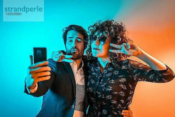 Party Lifestyle  ein verliebtes kaukasisches Paar macht ein Selfie auf einer Party mit orangen und blauen Lichtern