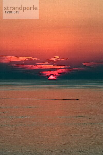 Ein kleines Boot fährt auf dem Meer bei romantischem Sonnenuntergang  die Sonne versinkt am Horizont im Meer