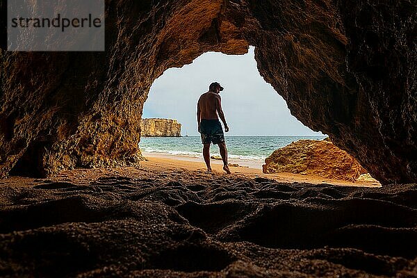 Ein Mann in einer natürlichen Höhle an der Algarve im Sommer am Strand von Praia da Coelha  Albufeira. Portugal