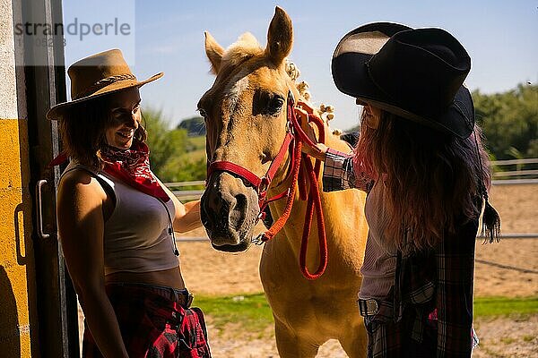 Silhouette von zwei Cowgirl Frauen  die mit einem Pferd in den Stall gehen  mit südamerikanischem Outfit