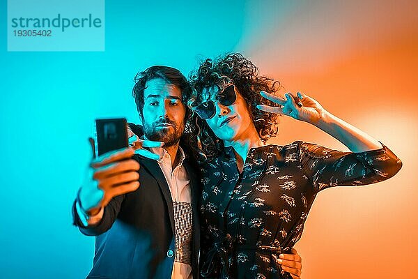 Party Lifestyle  ein kaukasisches Paar macht ein Selfie auf einer Party mit orangen und blauen Lichtern