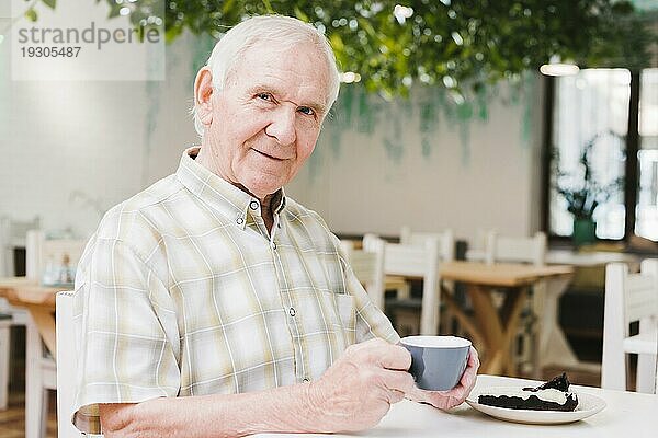 Älterer Mann trinkt Tee und schaut in die Kamera