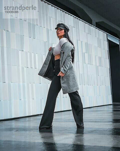 Modisches Posieren in der Stadt eines wunderschönen Latino Mädchens mit einem Lederhut und einem grauen Trenchcoat