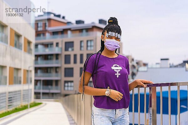 Internationaler Frauentag im Jahr der Coronaviruspandemie Covid 19. Dominikanische Frau mit feministischem lila Hemd und Gesichtsmaske in der Stadt