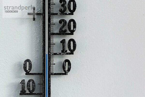 Klassisches schwarzes analoges Thermometer  das an einer weißen Wand hängt und eine blaue Temperaturskala von 10 Grad Celsius anzeigt