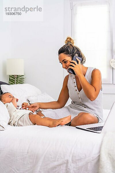 Junge kaukasische Mutter mit ihrem Sohn im Zimmer auf dem Bett. Die Mutter arbeitet von zu Hause aus und kümmert sich um ihr Kind  eine neue Normalität nach der Coronaviruspandemie Covid 19. Soziale Distanz