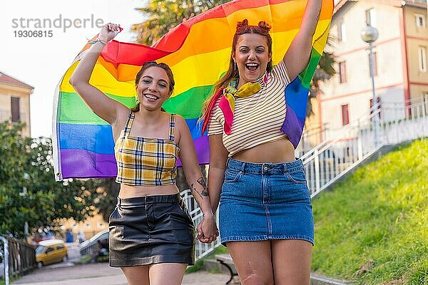 Eine Nahaufnahme von zwei jungen kaukasischen umarmen Frauen mit LGBT Stolz Flagge im Freien