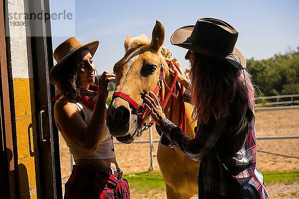 Silhouette von zwei Cowgirl Frauen  die mit einem Pferd in den Stall gehen  mit südamerikanischem Outfit