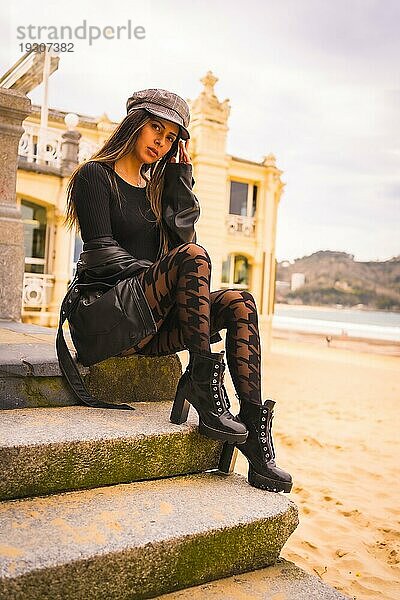 Lifestyle in der Stadt  Posing einer brünetten Kaukasierin in einem kurzen schwarzen Kleid und karierten Strümpfen neben einem Strand im Urlaub im Sommer