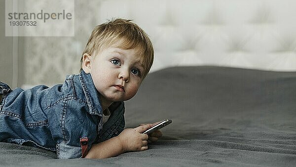 Junge liegt im Bett und hält ein Mobiltelefon