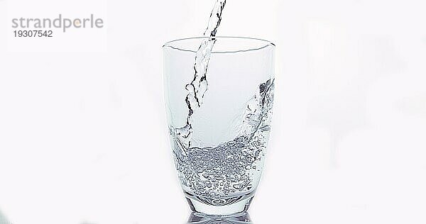 Wasser wird in Glas gegen weißen Hintergrund gegossen