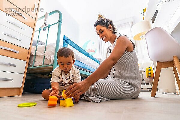 Junge kaukasische Mutter spielt mit ihr im Zimmer mit Spielzeug. Baby weniger als ein Jahr lernen die ersten Lektionen von ihrer Mutter. Mutter spielt mit ihrem Sohn spielen sitzen auf dem Boden