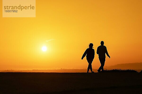 Schwarze Silhouetten eines Paares  das bei hellem Sonnenuntergang spazieren geht. Mittlere Aufnahme