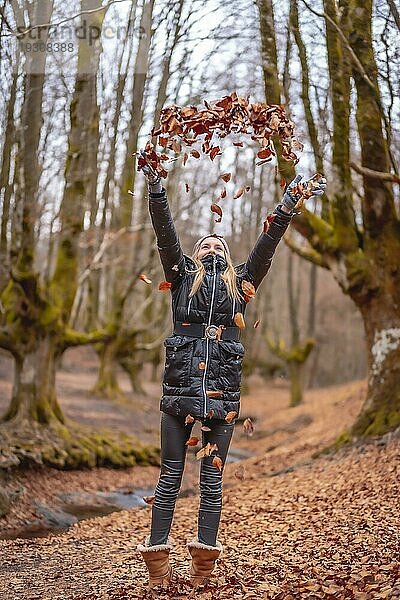 Sehr glückliches blondes Mädchen spielt mit Blättern in einem schönen Wald