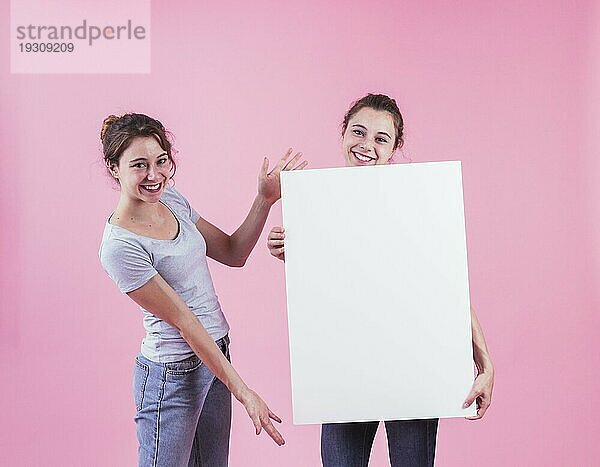 Frau präsentiert leeres Plakat  das von ihrem Freund gehalten wird  vor rosa Hintergrund