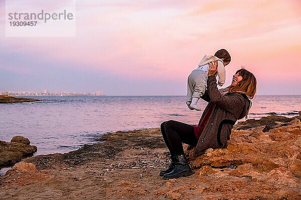 Lebensstil einer Familie am Strand  ein Baby hat Spaß mit seiner Mutter am Meer bei Sonnenuntergang