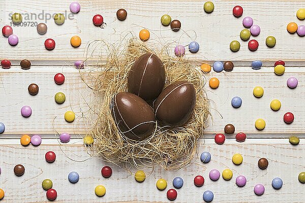 Bunte Edelstein Bonbons um Schokolade Ostereier Nest Holztisch umgeben