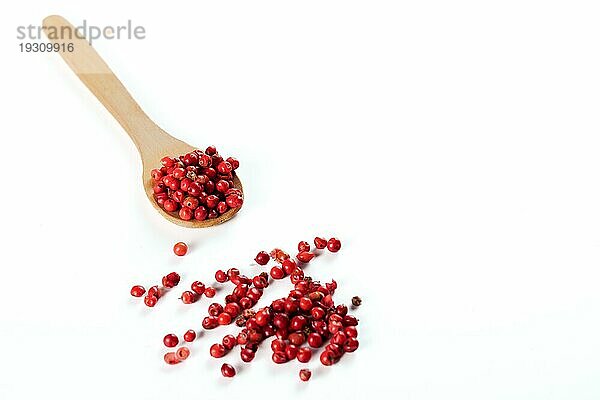 Holzlöffel mit rosa Pfefferkörner vor weißem Hintergrund und Kopie Raum