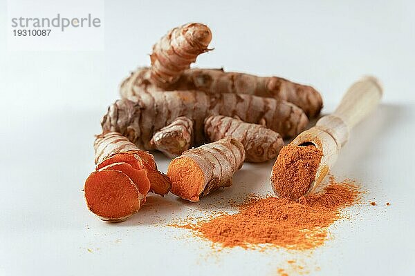 Frische Kurkumawurzel und gemahlene Kurkuma auf einem Holzlöffel vor weißem Hintergrund und Kopierraum